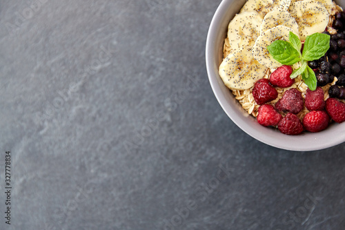 food and breakfast concept - oatmeal cereals in bowl with wild berries, banana and peppermint on slate stone table