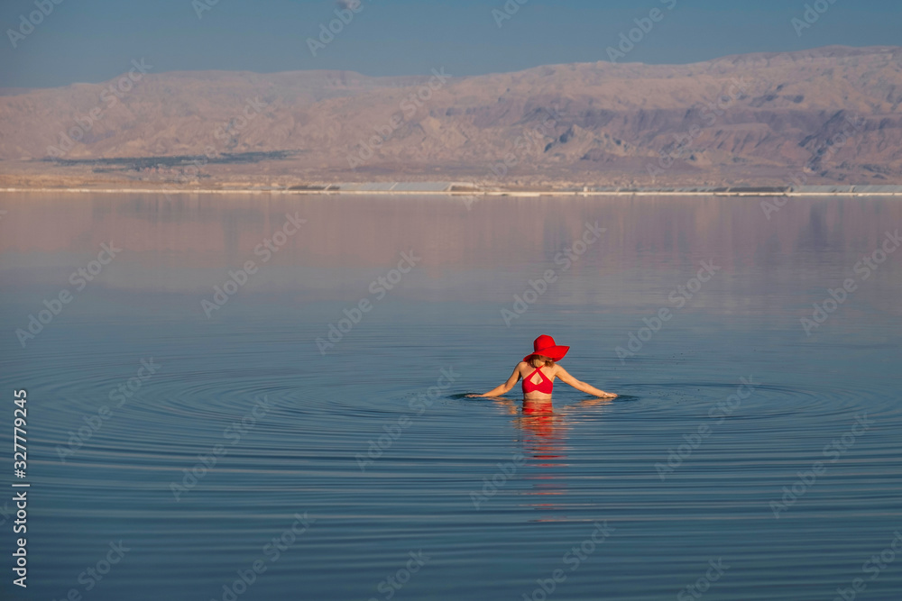 Woman swimming in Israel dead sea in red swimsuit and red hat. Perfectly blue water and sky. Summer scenic picture with copy space
