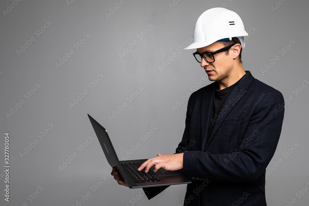 Smart young architect wearing glasses and safety helmet which hands holding a laptop to check his planned work isolated on white background Smart young architect wearing glasses and safety helmet which hands holding a laptop to check his planned work isolated on white background