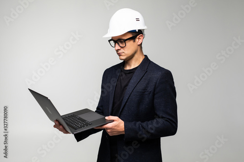 Smart young architect wearing glasses and safety helmet which hands holding a laptop to check his planned work isolated on white background