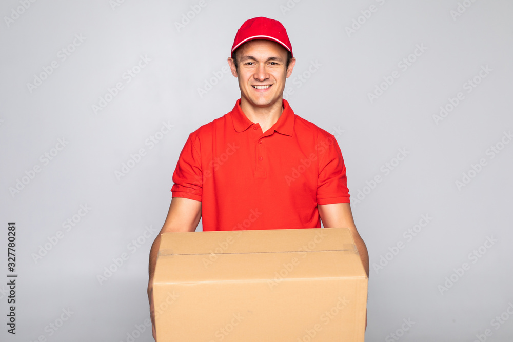 Excited happy young delivery man in red cap standing with parcel post box isolated over white background. Excited happy young delivery man in red cap standing with parcel post box isolated over white background.