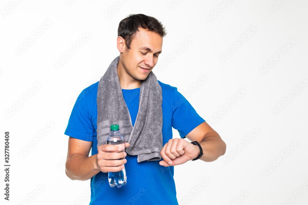 Young handsome fitness man look at smart watch after training with bottle and towel isolated on white background Young handsome fitness man look at smart watch after training with bottle and towel isolated on white background