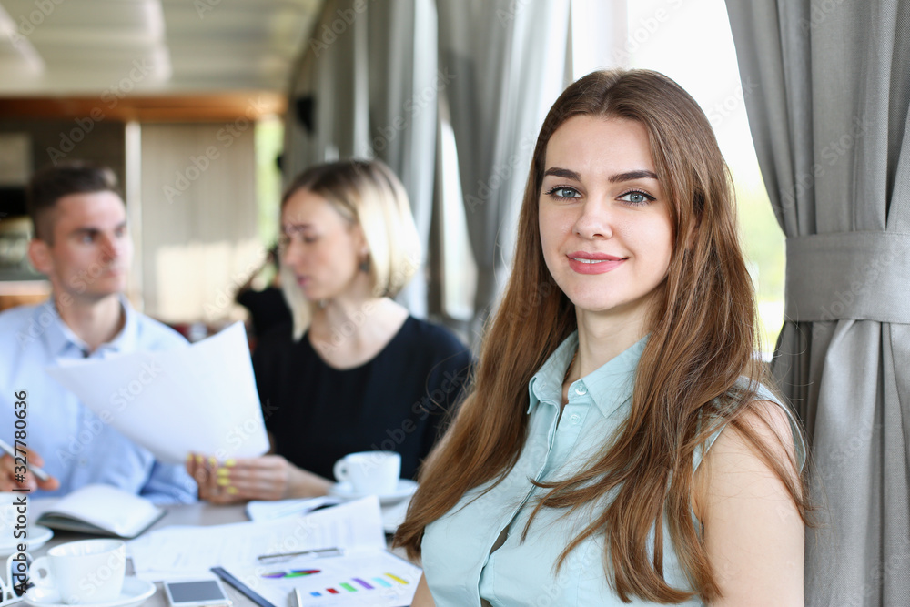 Beautiful smiling cheerful girl at cafe look in camera with colleagues group in background. White collar worker at workspace job offer modern lifestyle client visit profession train concept Beautiful smiling cheerful girl at cafe look in camera with colleagues group in background. White collar worker at workspace job offer modern lifestyle client visit profession train concept