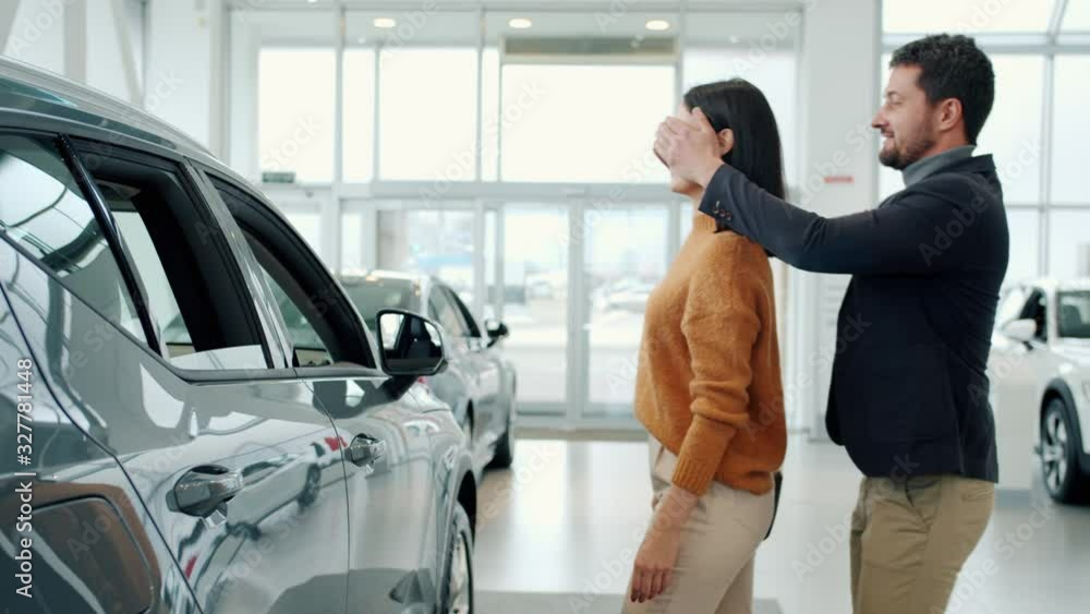 Businessman is buying new car for attractive young girlfriend making exciting surprise, happy lady is hugging boyfriend and laughing enjoying present. Businessman is buying new car for attractive young girlfriend making exciting surprise, happy lady is hugging boyfriend and laughing enjoying present.