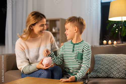 money, family and people concept - happy smiling mother and thrifty little son putting euro coin to piggy bank at home