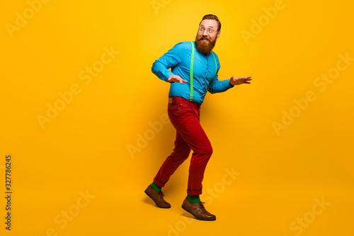 Full length photo of attractive guy slow hush steps hiding girlfriend making surprise visit wear blue shirt green suspenders red pants socks footwear isolated yellow color background