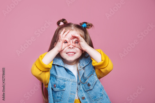 Funny little girl do funny double OK sign as glasses on pink background photo