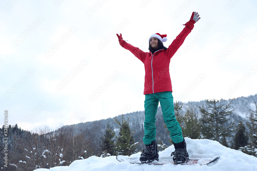 Young snowboarder wearing Santa hat on snowy hill. Winter vacation