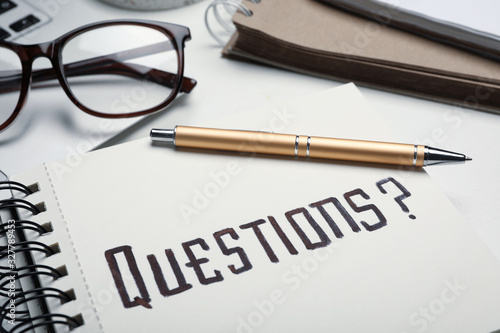 Notebook with word QUESTIONS and pen on table, closeup