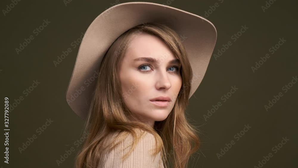 A young beautiful elegant woman in a beige sweater and fedora with fields poses against a green olive background. A close-up of the face. Romantic and sensual lady. A young beautiful elegant woman in a beige sweater and fedora with fields poses against a green olive background. A close-up of the face. Romantic and sensual lady.