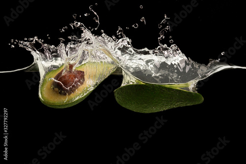 Yummy avocado cut in half and water splashes on black background