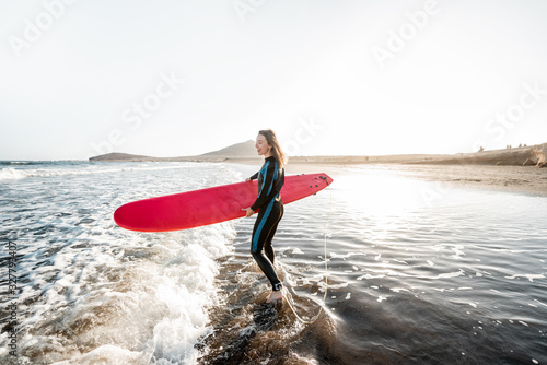 Young surfer in wetsuit running with surfboard to the sea. Summer activities and active lifestyle concept