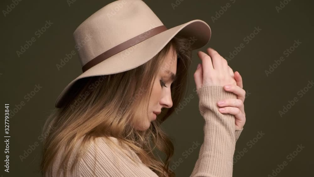 A young beautiful elegant woman in a beige sweater and fedora with fields poses against a green olive background. A close-up of the face. Romantic and sensual lady. A young beautiful elegant woman in a beige sweater and fedora with fields poses against a green olive background. A close-up of the face. Romantic and sensual lady.