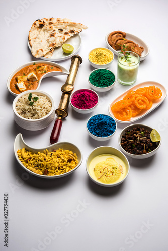 Happy Holy concept showing Indian assorted lunch food like paneer butter masala, naan, jeera rice, black chana fry, jalebi, fujiyama, thandai and Farsan with holi colours and pichkari 