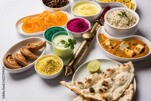 Happy Holy concept  showing Indian assorted lunch food like paneer butter masala, naan, jeera rice, black chana fry, jalebi, fujiyama, thandai and Farsan with holi colours and pichkari  photo