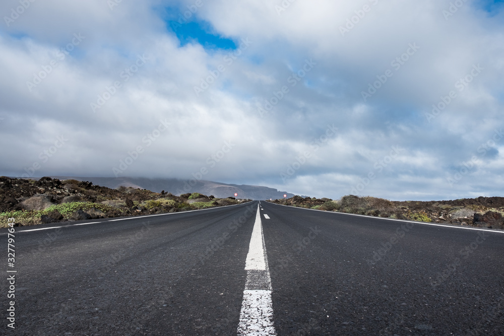 Endless road to Timanfaya National park in Lanzarote, Canary Ispands, Spain, Europe, Africa. Volcanic, black sand, harsh, tough, inhospitable, dry, sub-tropical, desert landscape.