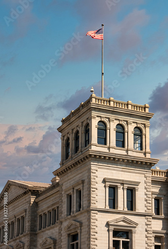 An old granite stone block building under blue skies with American flag