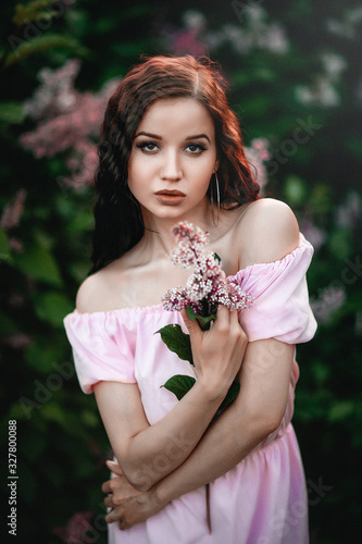 Beautiful young girl in a pink dress posing in flowers. Posing and enjoying the spring. Art work of romantic woman .Pretty tenderness model looking at camera. Gardening.. photo