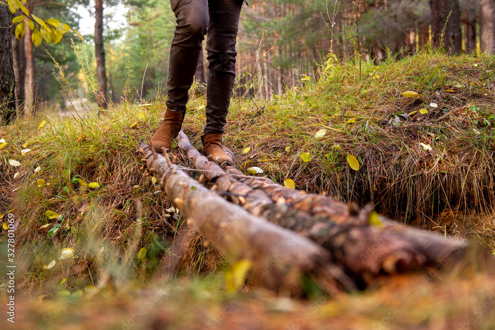 An unreliable rickety bridge over a pit of pine logs. Crossing the moat in the forest. A man crosses a dangerous bridge. An unreliable rickety bridge over a pit of pine logs. Crossing the moat in the forest. A man crosses a dangerous bridge.