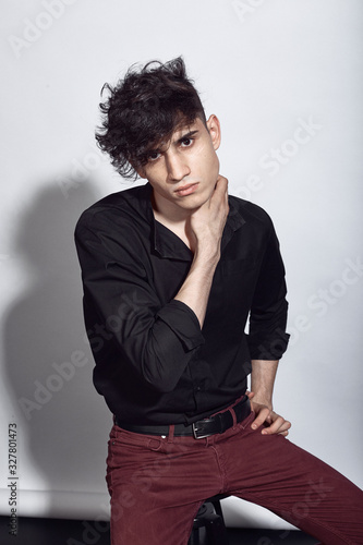 Young guy in a black shirt similar to Adriano Celentano posing on a white background. Fashion portrait photo