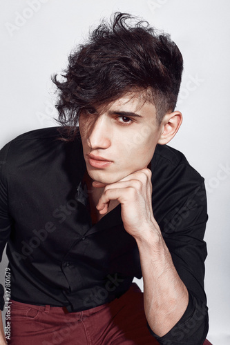 Young guy in a black shirt similar to Adriano Celentano posing on a white background. Fashion portrait
