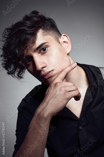 Young guy in a black shirt similar to Adriano Celentano posing on a white background. Fashion portrait photo