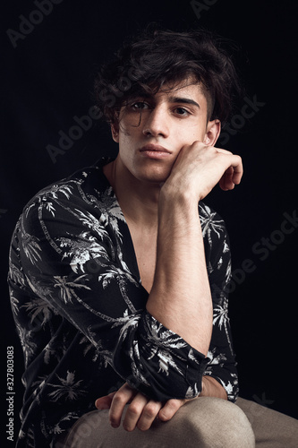 Young guy in a black shirt similar to Adriano Celentano posing on a black background. Fashion portrait photo