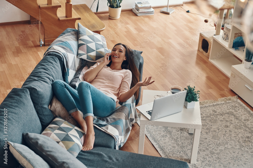 Top view of beautiful young woman in casual clothing talking on the phone and smiling while spending time at home Top view of beautiful young woman in casual clothing talking on the phone and smiling while spending time at home