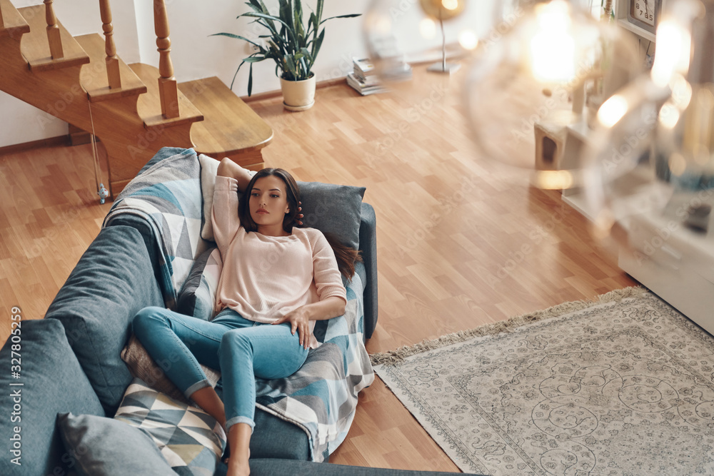 Obraz premium Top view of relaxed young woman in casual clothing resting on sofa while spending time at home