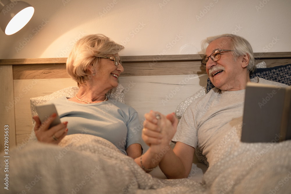 Obraz premium Happy mature couple holding hands while communicating in bed in the evening.