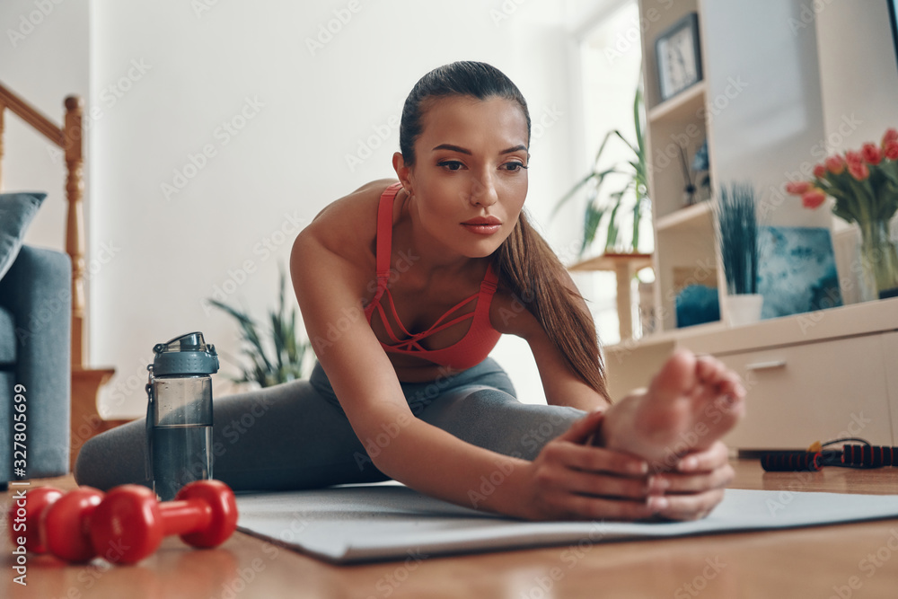 Flexible fit young woman in sports clothing stretching on exercise mat while spending time at home Flexible fit young woman in sports clothing stretching on exercise mat while spending time at home