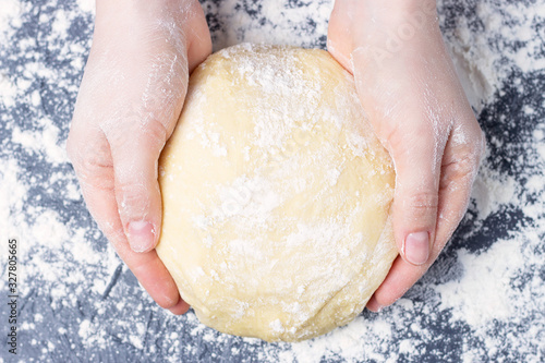 Female hands hold a round dough on gray background, top view.