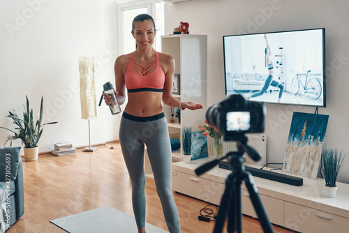 Beautiful young woman in sports clothing working out and smiling while making social media video