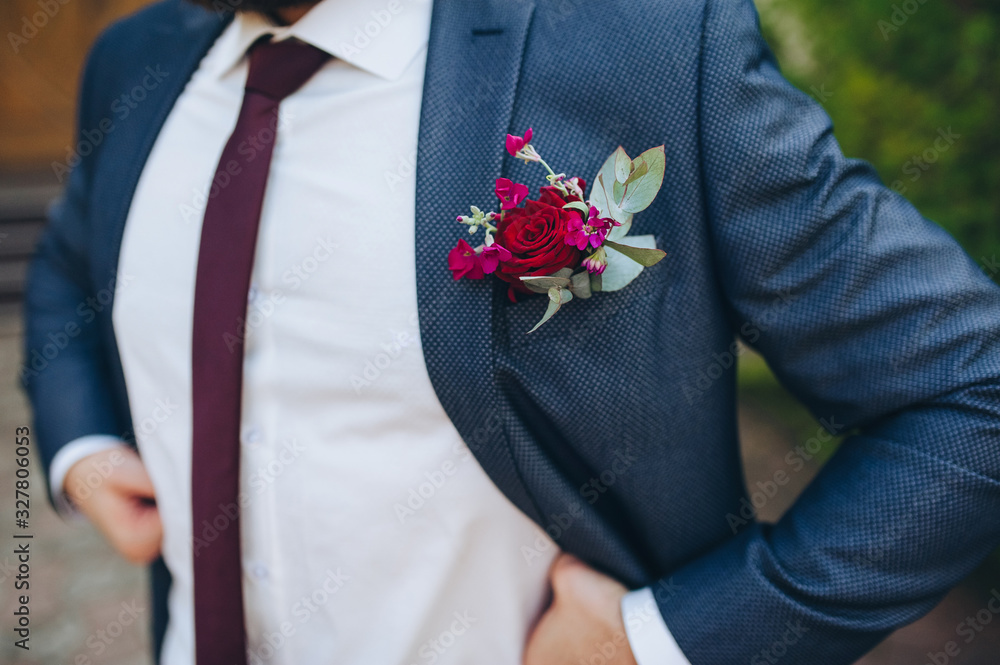 Closeup of groom's boutonniere and blue suit. Flowers of rose, white shirt and burgundy tie. Closeup of groom's boutonniere and blue suit. Flowers of rose, white shirt and burgundy tie.