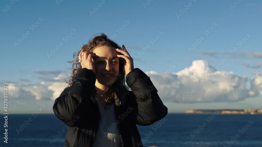 Pretty brunette tucks her windswept hair behind her ears with the beautiful blue Pacific ocean in the background. Pretty brunette tucks her windswept hair behind her ears with the beautiful blue Pacific ocean in the background.