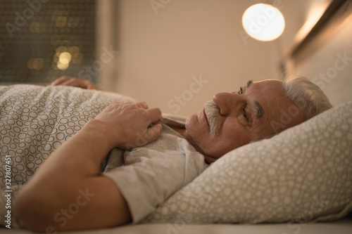 Distraught senior man thinking of something while lying down in bed at night.