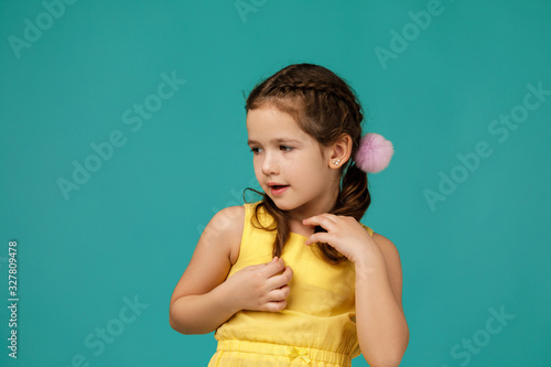 Cute shy little child girl in yellow dress on blue background. Human emotions