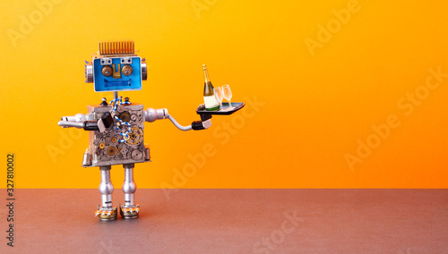 Robotic food delivery service concept. Laughing robot waiter holds tray with wine glasses, bottle of champagne. Autonomous steampunk mechanical toy on orange wall, brown floor background. copy space.