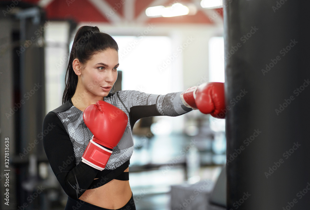 Self defense class. Young woman in boxing gloves punching ball in gym
