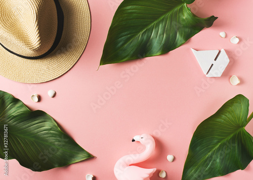 Vacation flat lay frame with hut, laeves, flamingo and other accessories on pink background photo