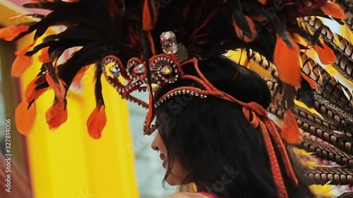 Beautiful girl bright colorful carnival costume decorated with rhinestones dancing samba against the background of a yellow building. Half-naked cabaret diva plastically moves. Brazilian carnival