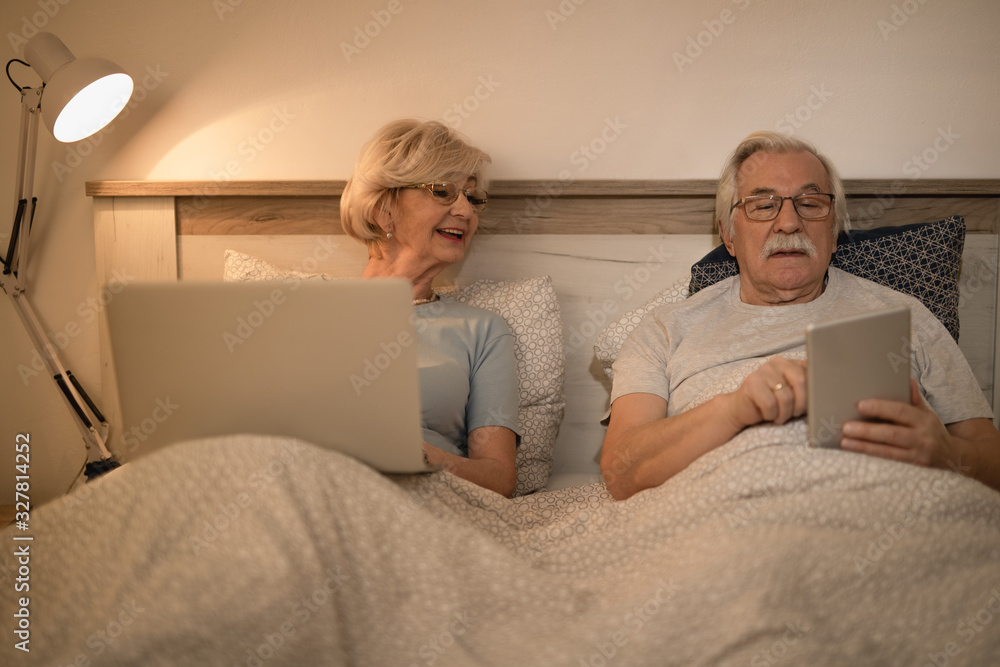 Senior couple using wireless technology while lying in bed at night. Senior couple using wireless technology while lying in bed at night.