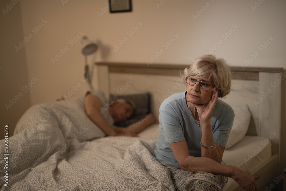 Worried mature woman thinking of something while sitting in bedroom at night. Worried mature woman thinking of something while sitting in bedroom at night.
