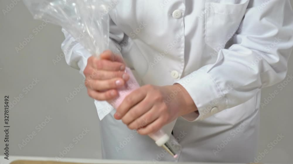 A female baker squeezes cream from a cone for baking marshmallows and meringues and makarons, In white uniform. A female baker squeezes cream from a cone for baking marshmallows and meringues and makarons, In white uniform.