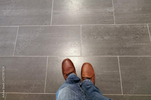 Legs in jeans and red shoes against the background of the tiled floor