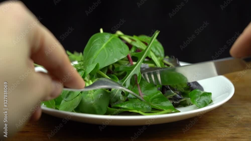 Slow motion shot of fresh salad with rucola, purple lettuce, spinach, frisee and chard leaf on a white plate with fork and knife. Diet and healthy eating concept Slow motion shot of fresh salad with rucola, purple lettuce, spinach, frisee and chard leaf on a white plate with fork and knife. Diet and healthy eating concept