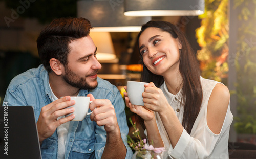 Lovely millennial couple enjoying coffee sitting in coffeehouse