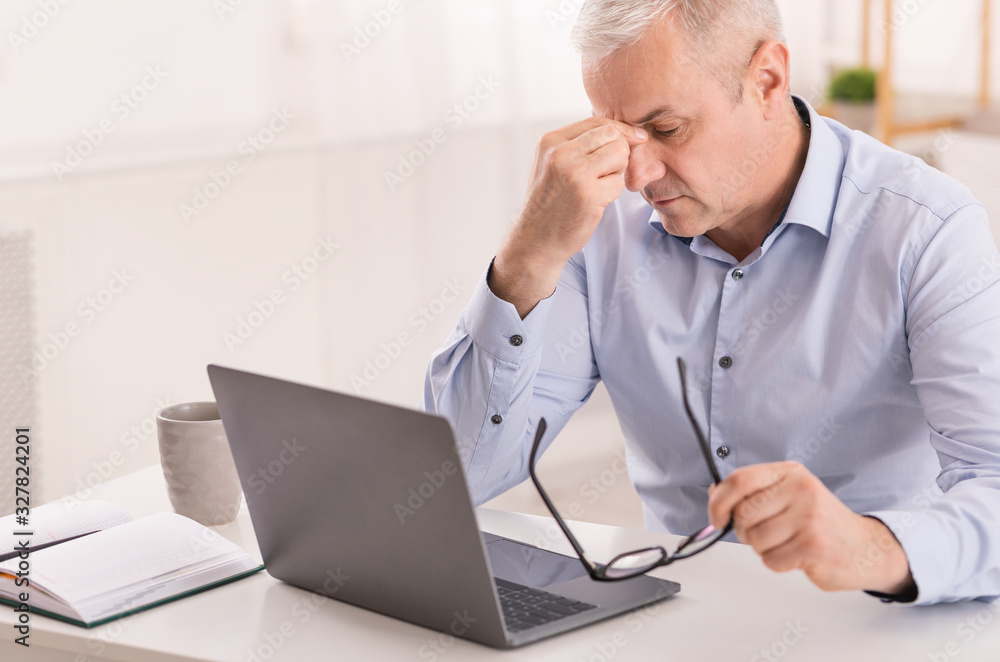 Senior manager massaging nose while using laptop