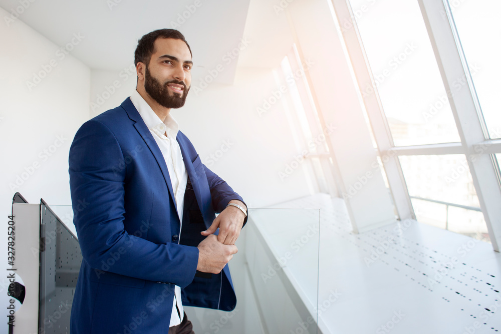 Successful handsome businessman in a blue suit at the workplace looks out the window, portrait of a manager at work Successful handsome businessman in a blue suit at the workplace looks out the window, portrait of a manager at work