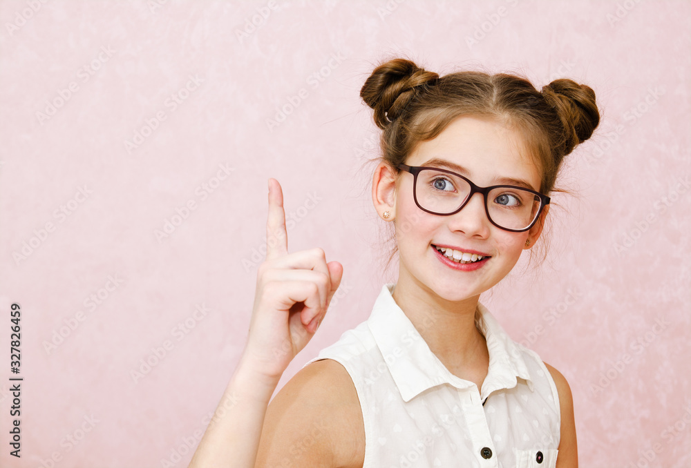 Portrait of funny smiling little girl child wearing glasses with finger up isolated on a pink background